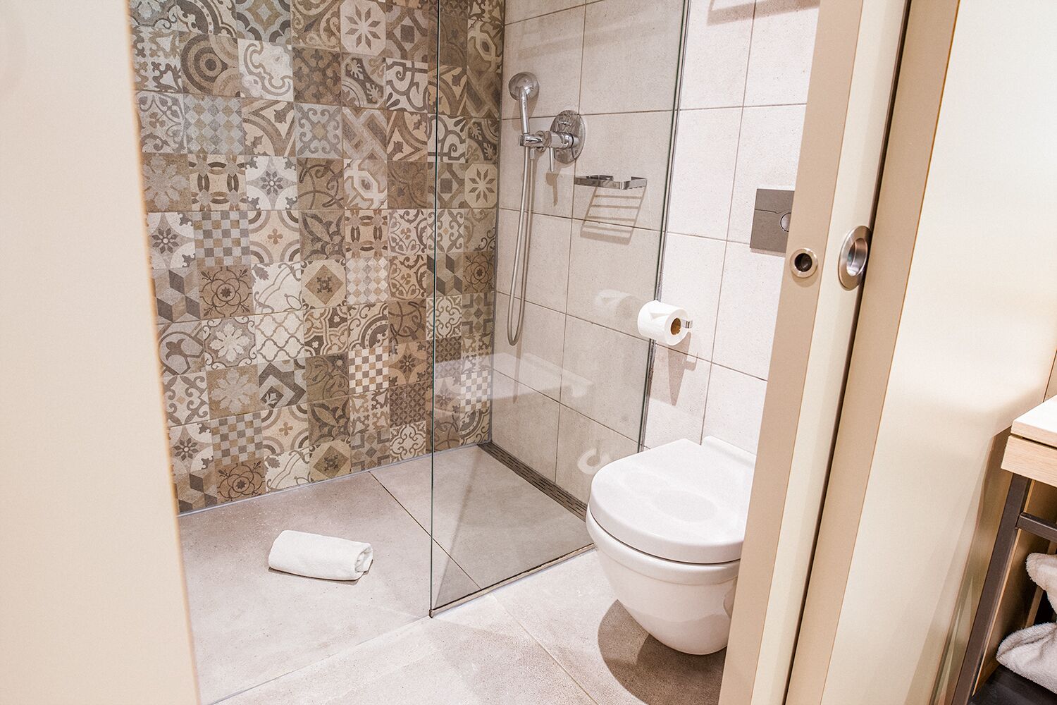 A bathroom with a shower, toilet, and patterned tiles.
