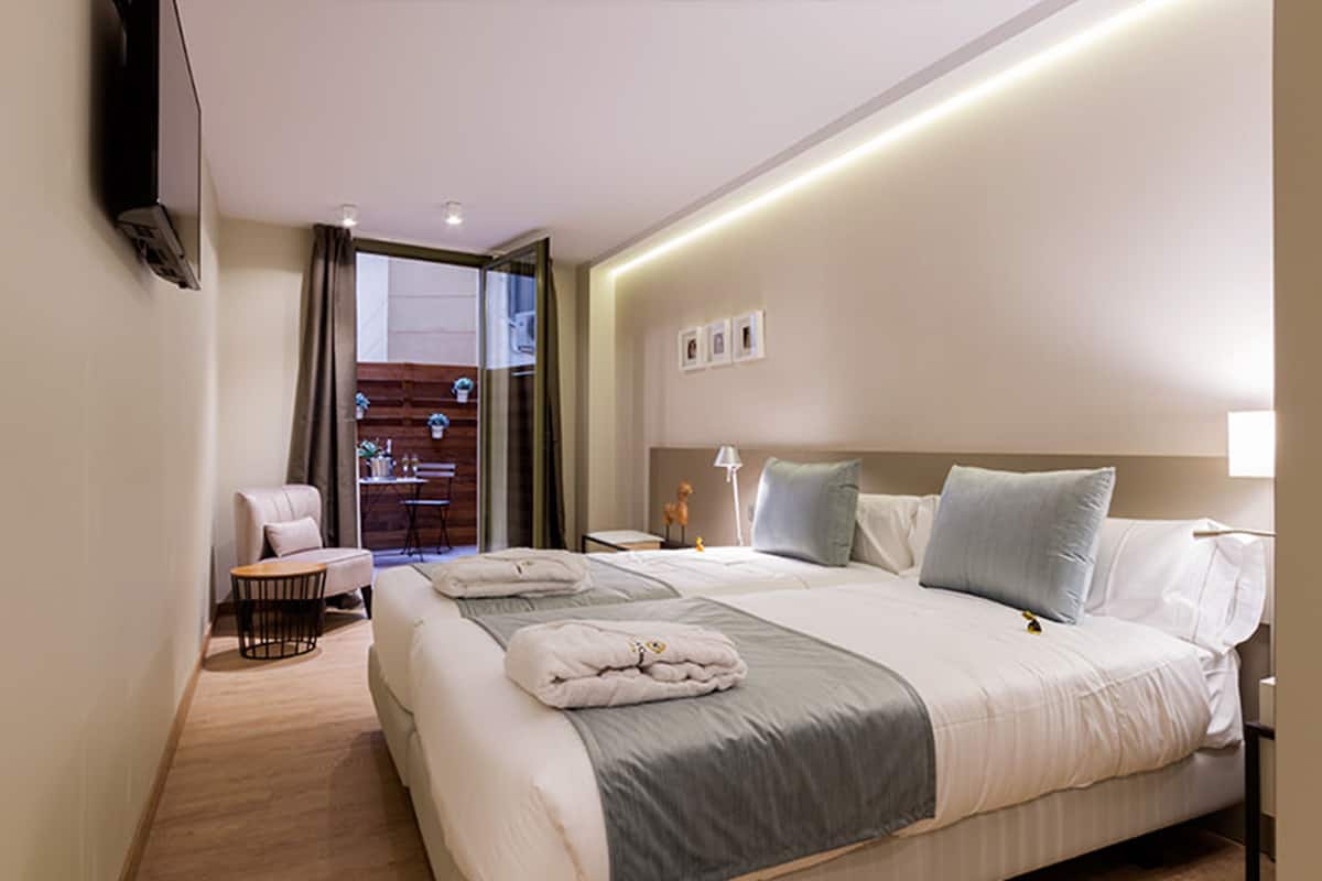 A hotel room with a large bed, a chair, a small table, and a TV mounted on the wall.