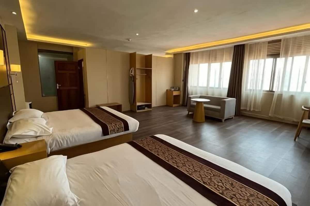Habitación de hotel con dos camas, un área de estar con una mesa, un armario y un baño.
