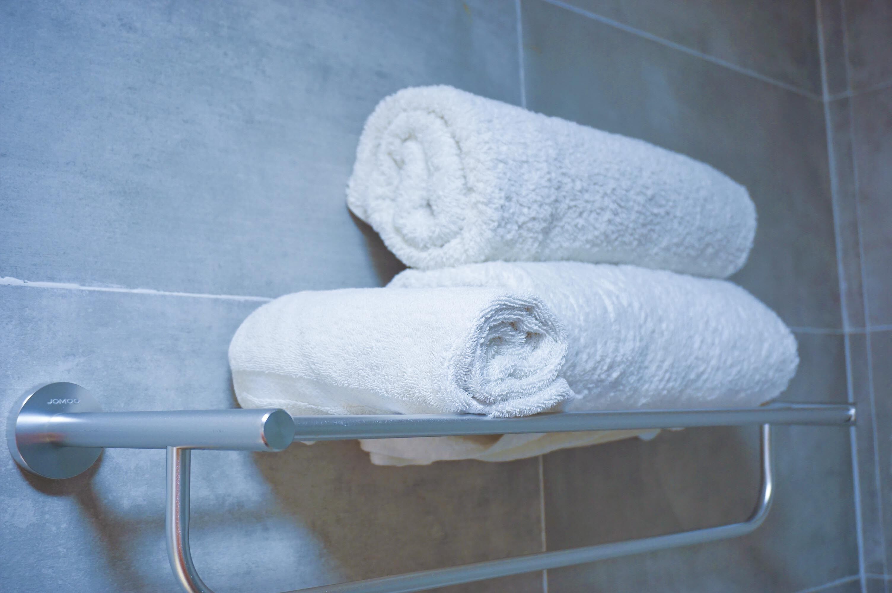 Two white towels rolled and placed on a metal towel rack in a bathroom with tiled walls.
