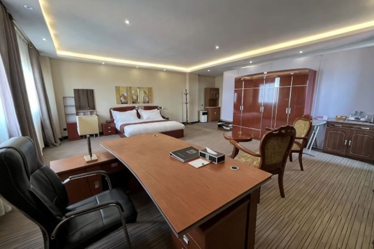 A hotel room with a bed, desk, chairs, a wardrobe, and a small kitchenette.