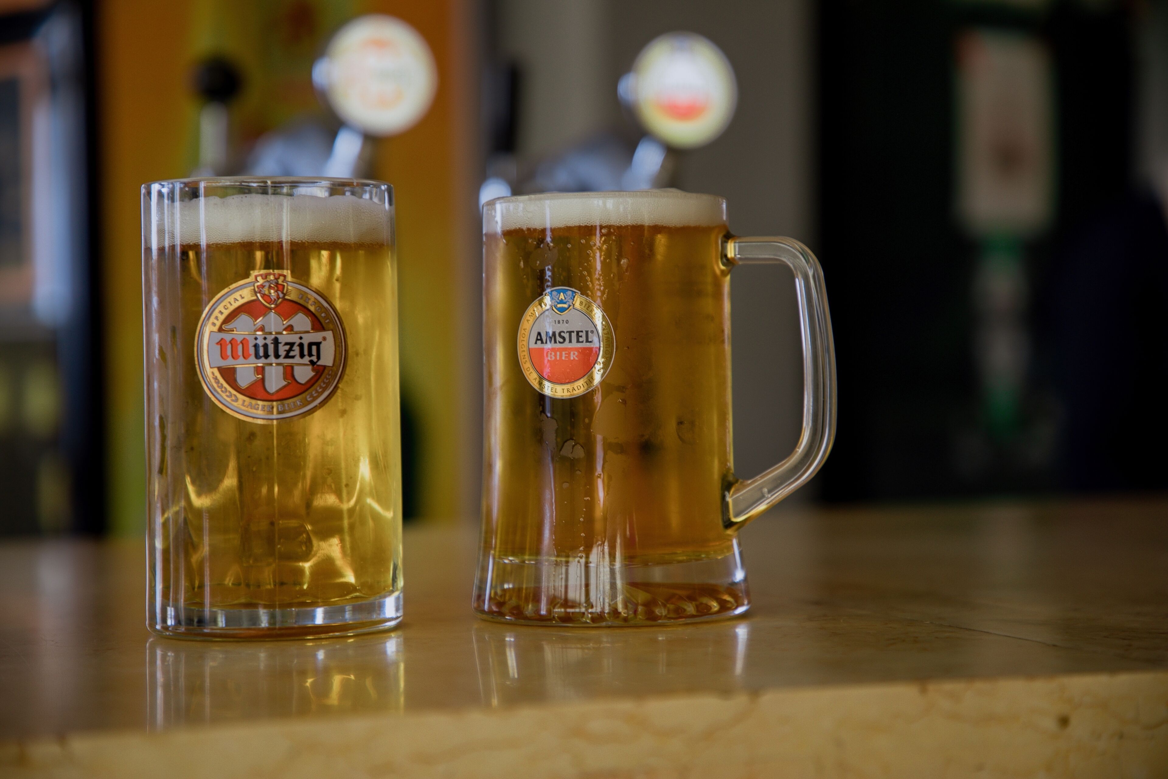 Zwei Bierkrüge mit Etiketten auf einer spiegelnden Oberfläche.