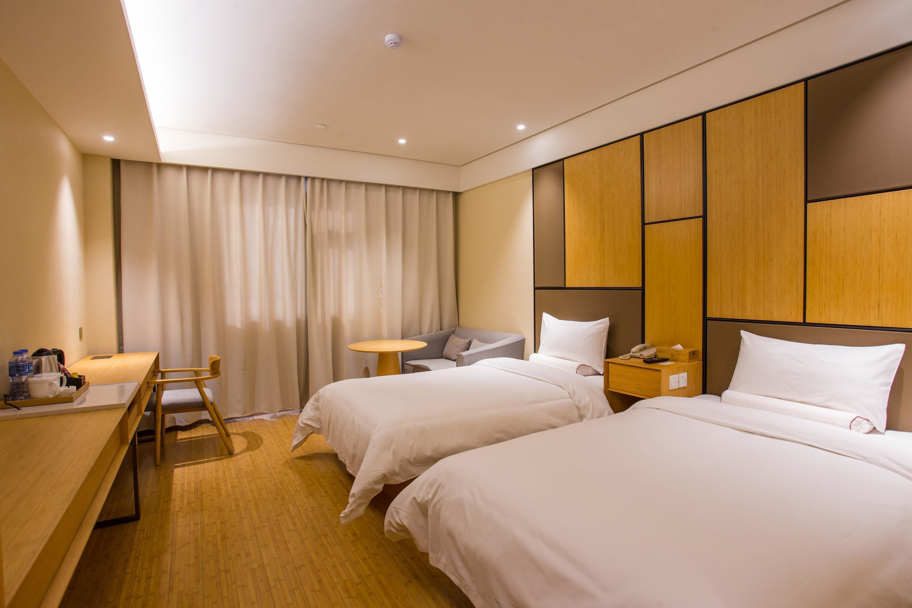 A hotel room with two beds, a desk with a chair, a small round table, and a nightstand with a phone.
