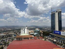 A cityscape with a prominent modern building, a parking lot, and a view of distant mountains.