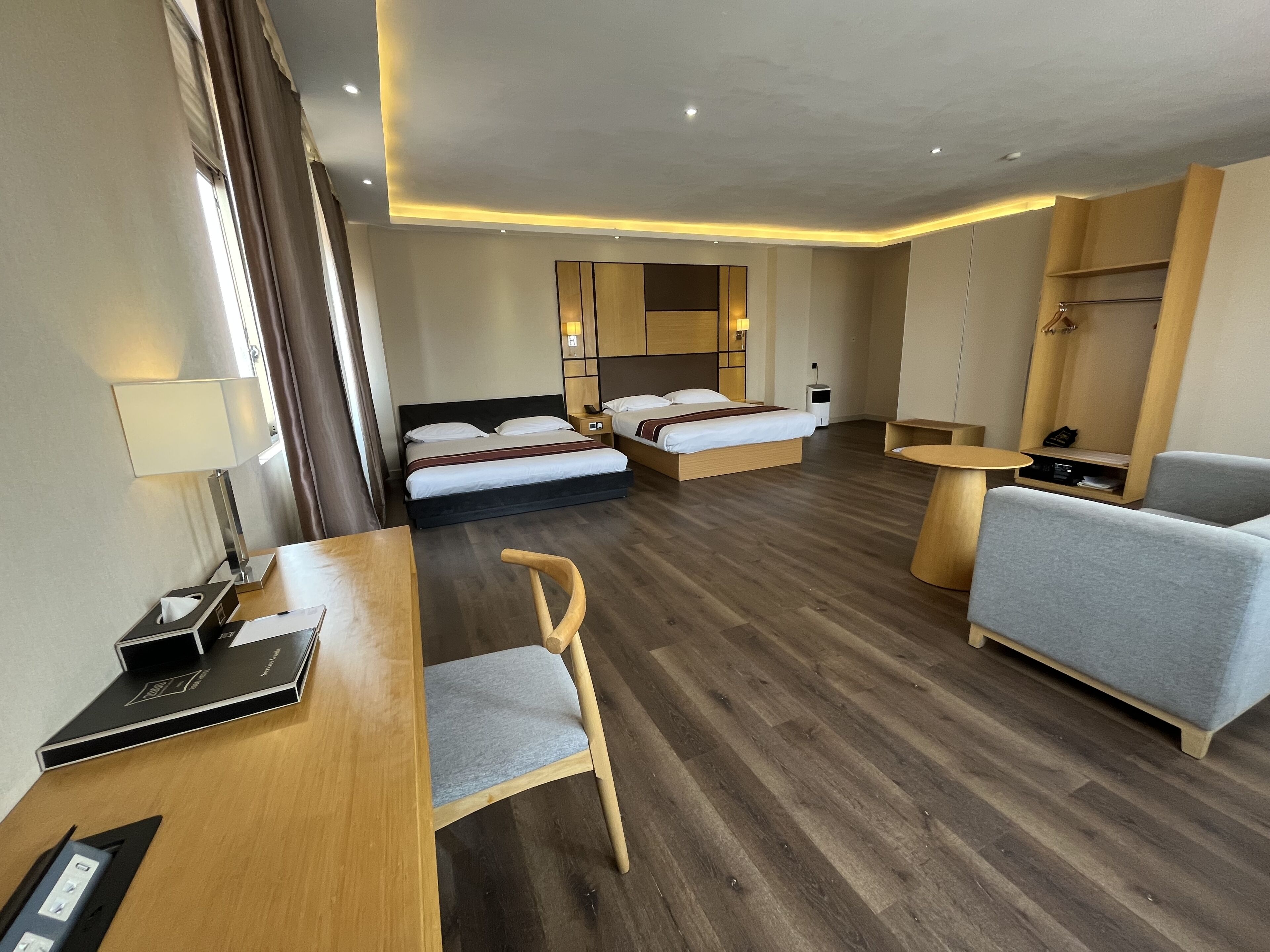 A hotel room with a wooden floor, a bed with white linens, a desk with a lamp, a chair, a sofa, and a small table.