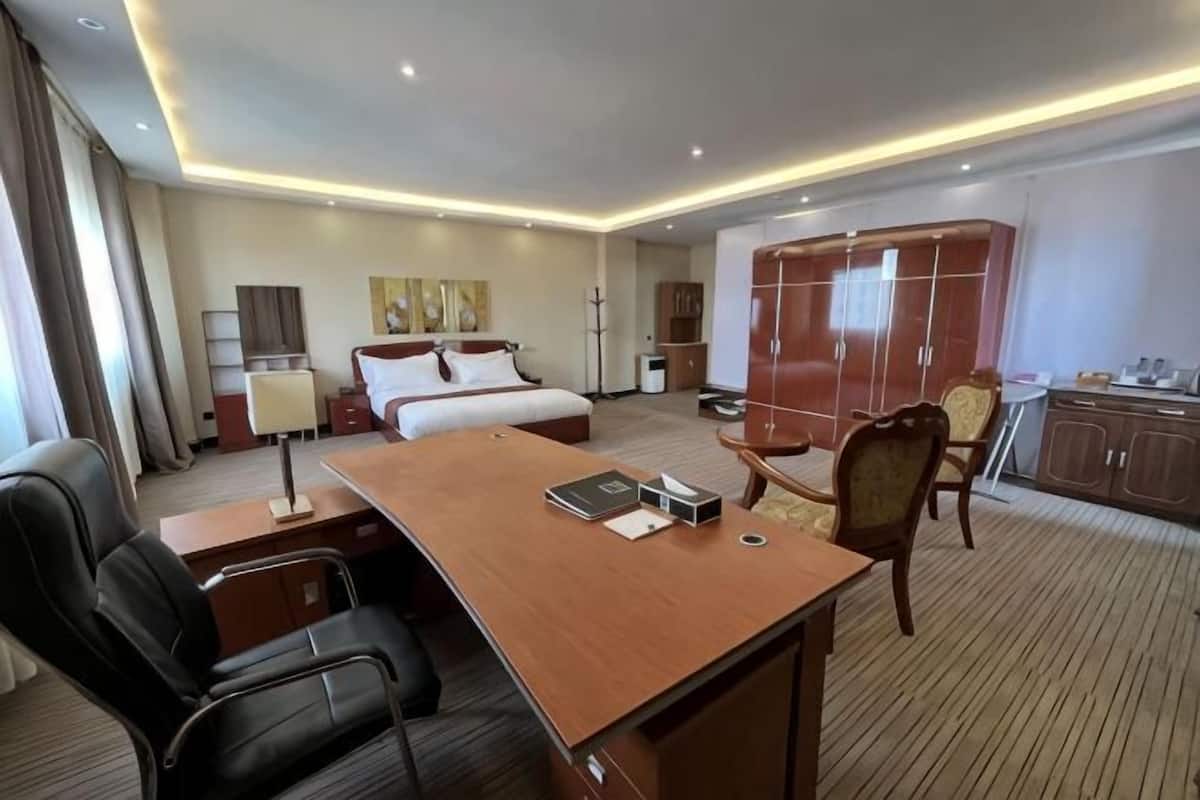 Una habitación de hotel con cama, escritorio, sillas, armario y una pequeña cocina.
