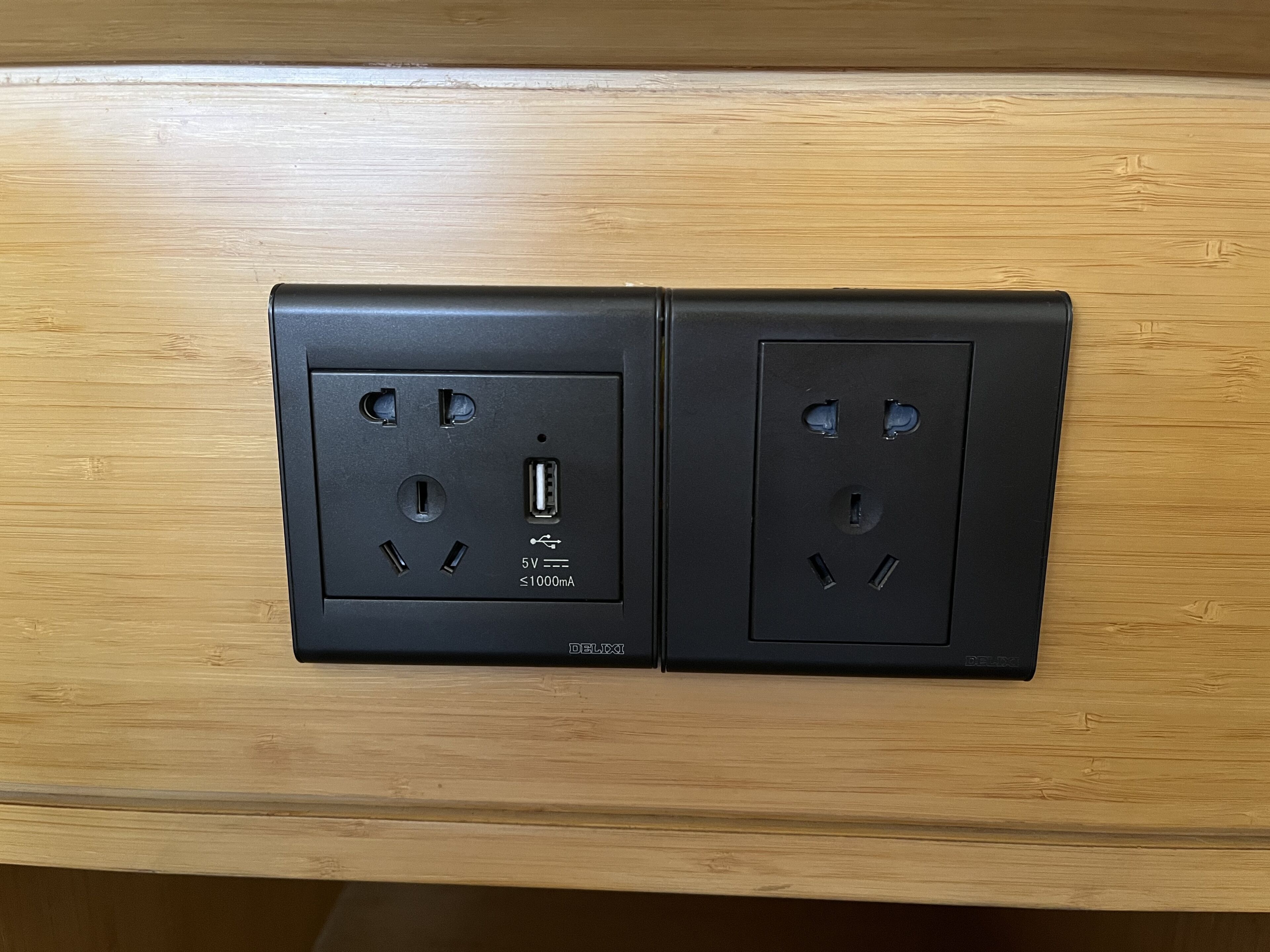 A black electrical outlet with a USB port and a 5V socket on a wooden surface.