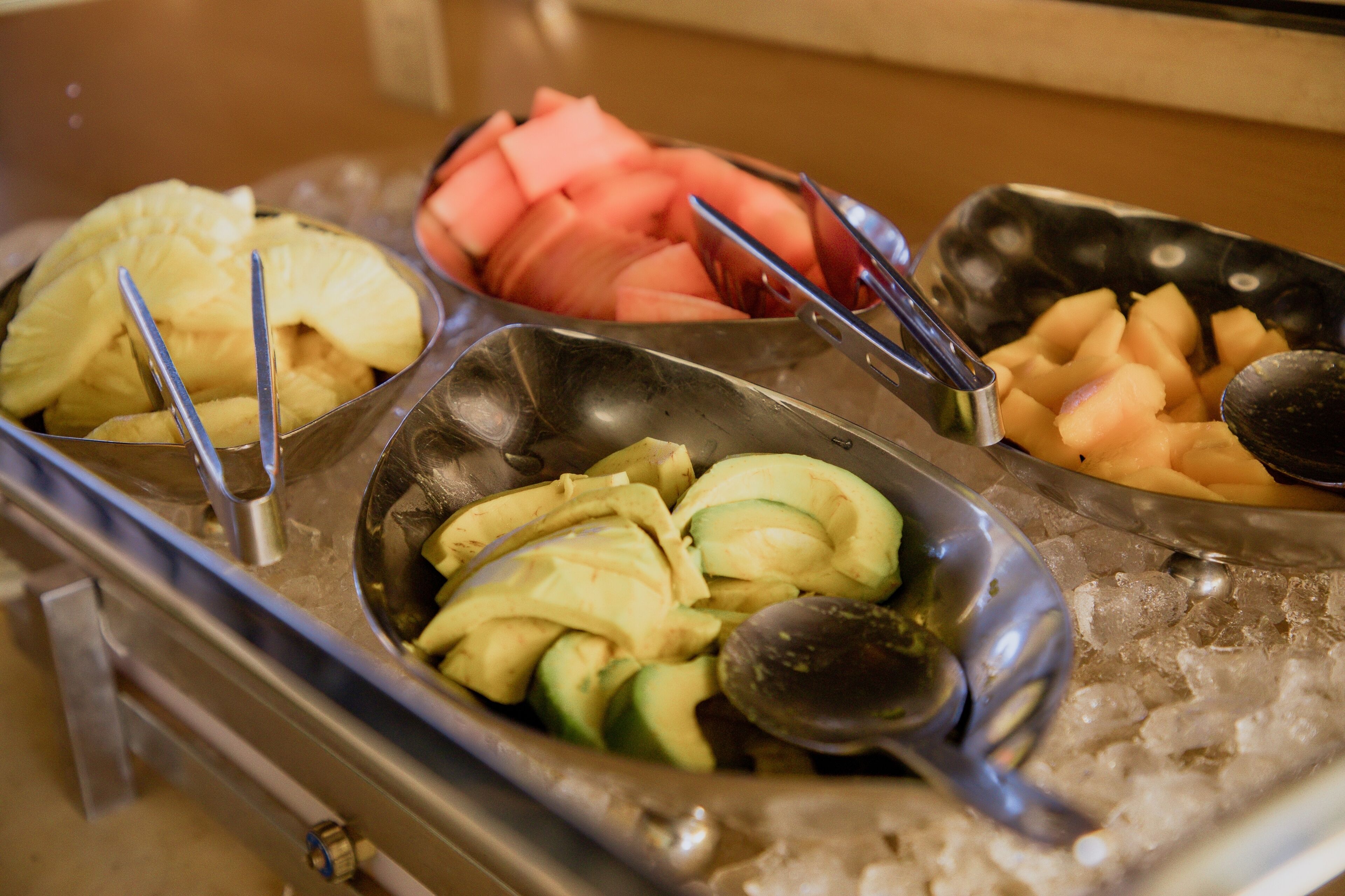 A buffet with various fruits and vegetables, including pineapple, watermelon, and avocado, served on a bed of ice.