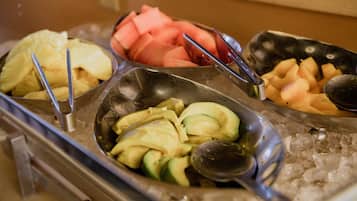 A buffet with various fruits and vegetables, including pineapple, watermelon, and avocado, served on a bed of ice.