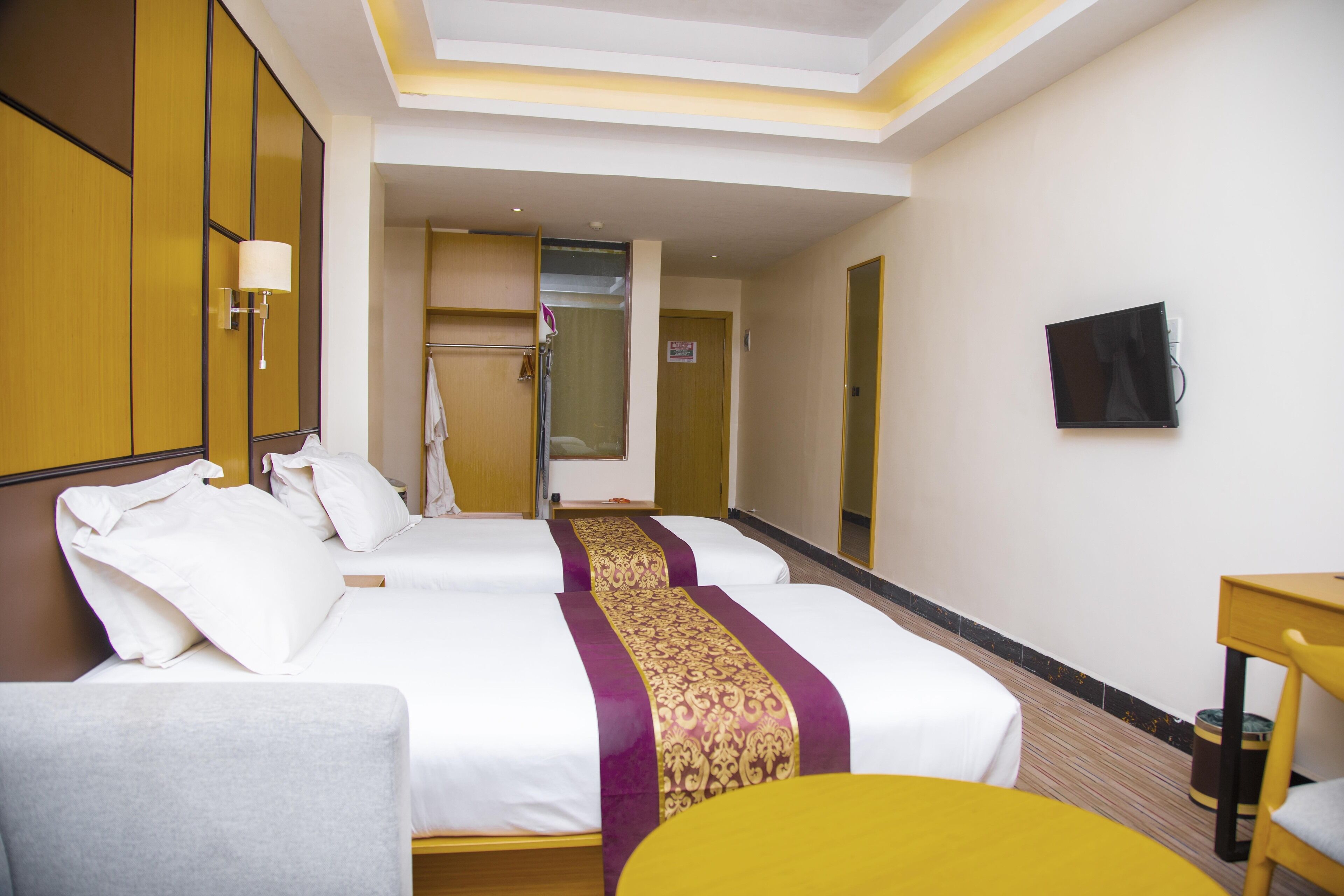 A hotel room with two beds, a desk, a chair, a TV, and a bathroom visible through an open door.