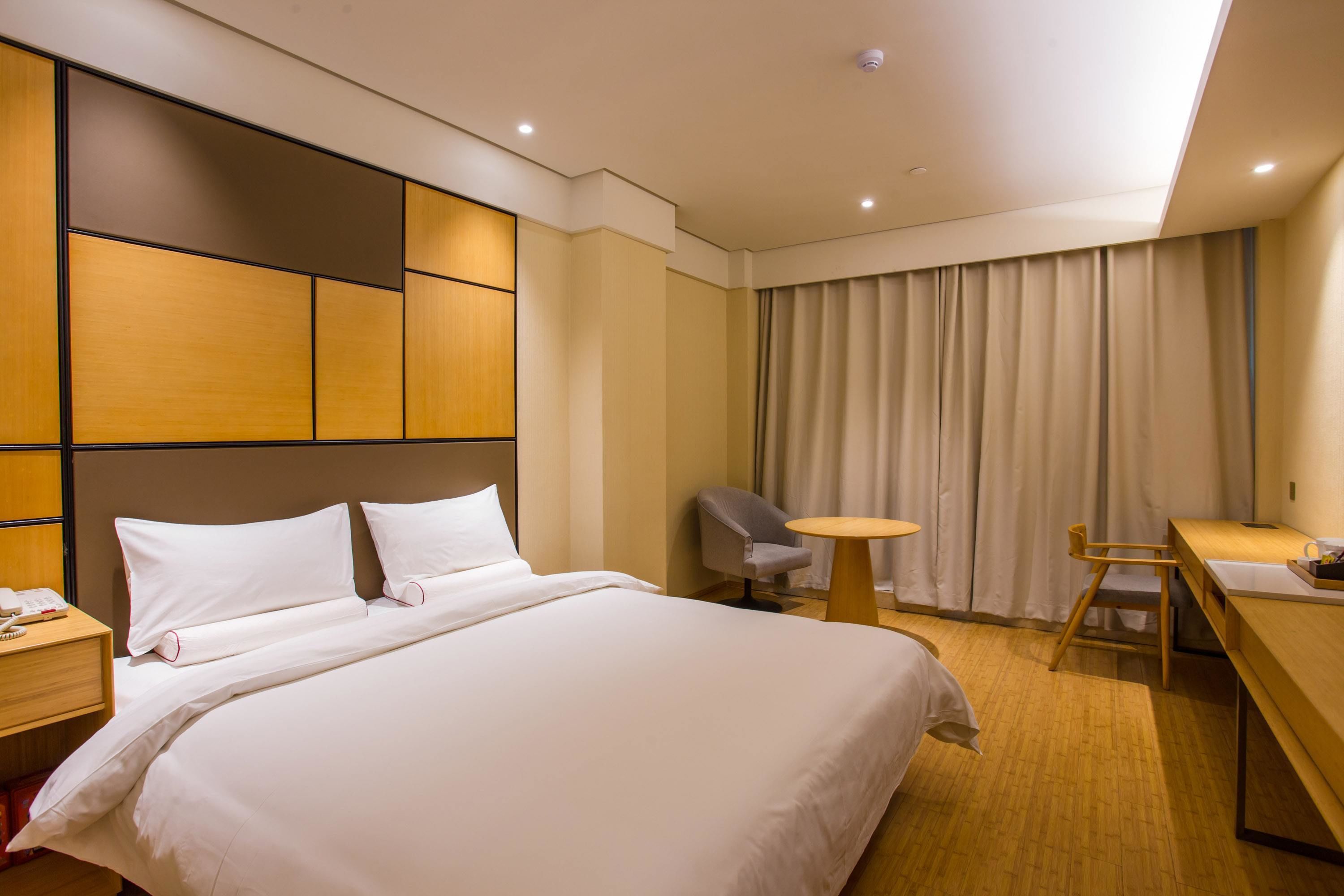 A hotel room with a large bed, a desk, a chair, and a small table.