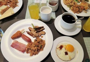 A breakfast setting with plates of food, including fried rice, eggs, and sausages, along with cups of coffee and a glass of juice.