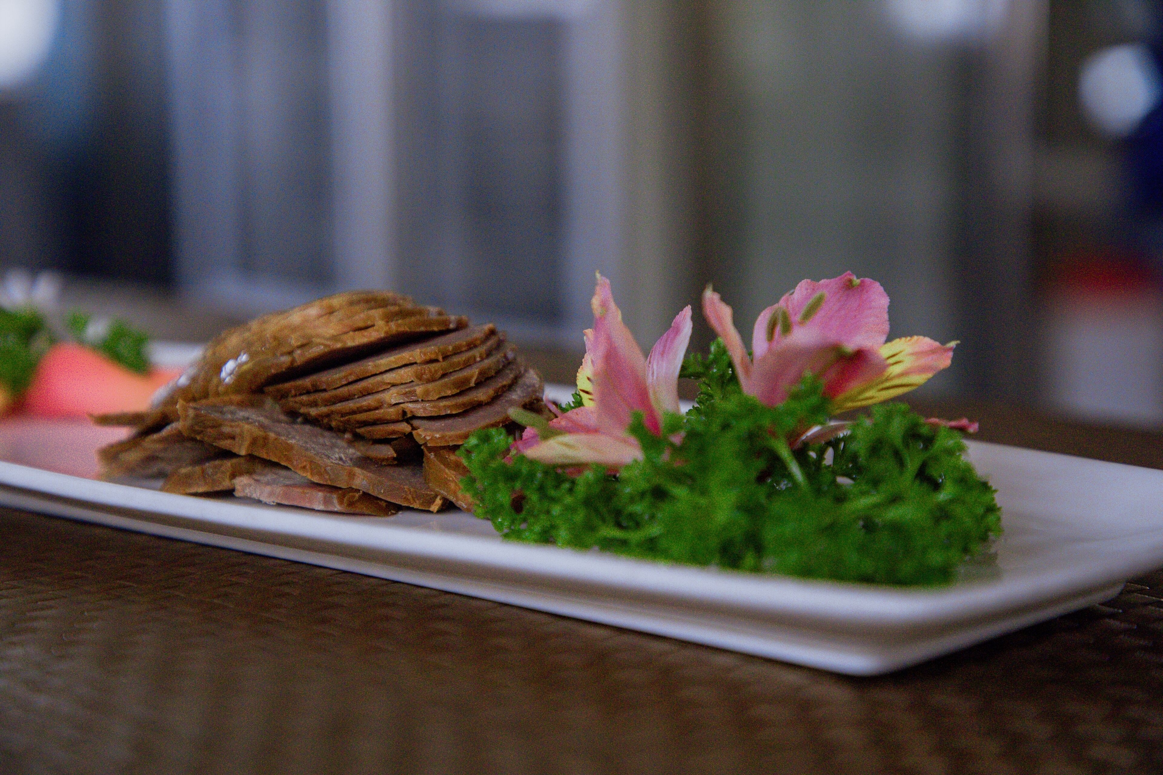Un plato rectangular blanco con una pila de rebanadas de pan marrón, lechuga verde y flores rosadas.