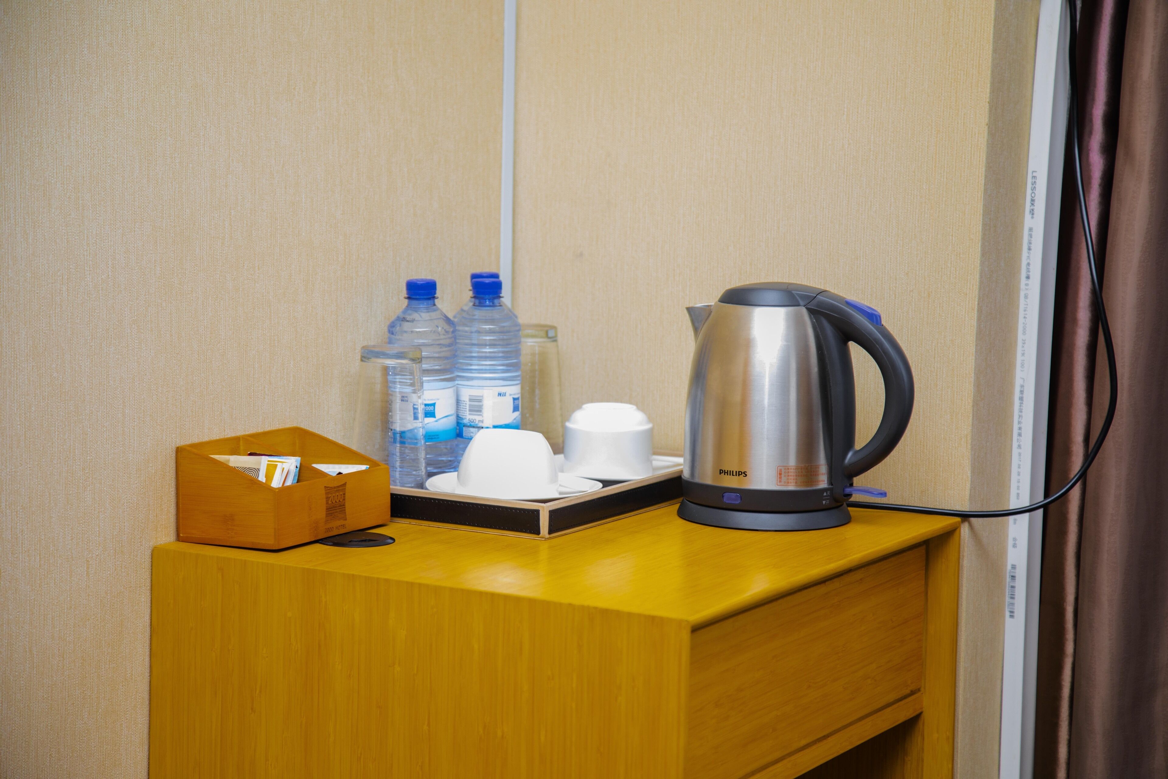 A hotel room with a wooden desk, a coffee maker, water bottles, and a tissue box.