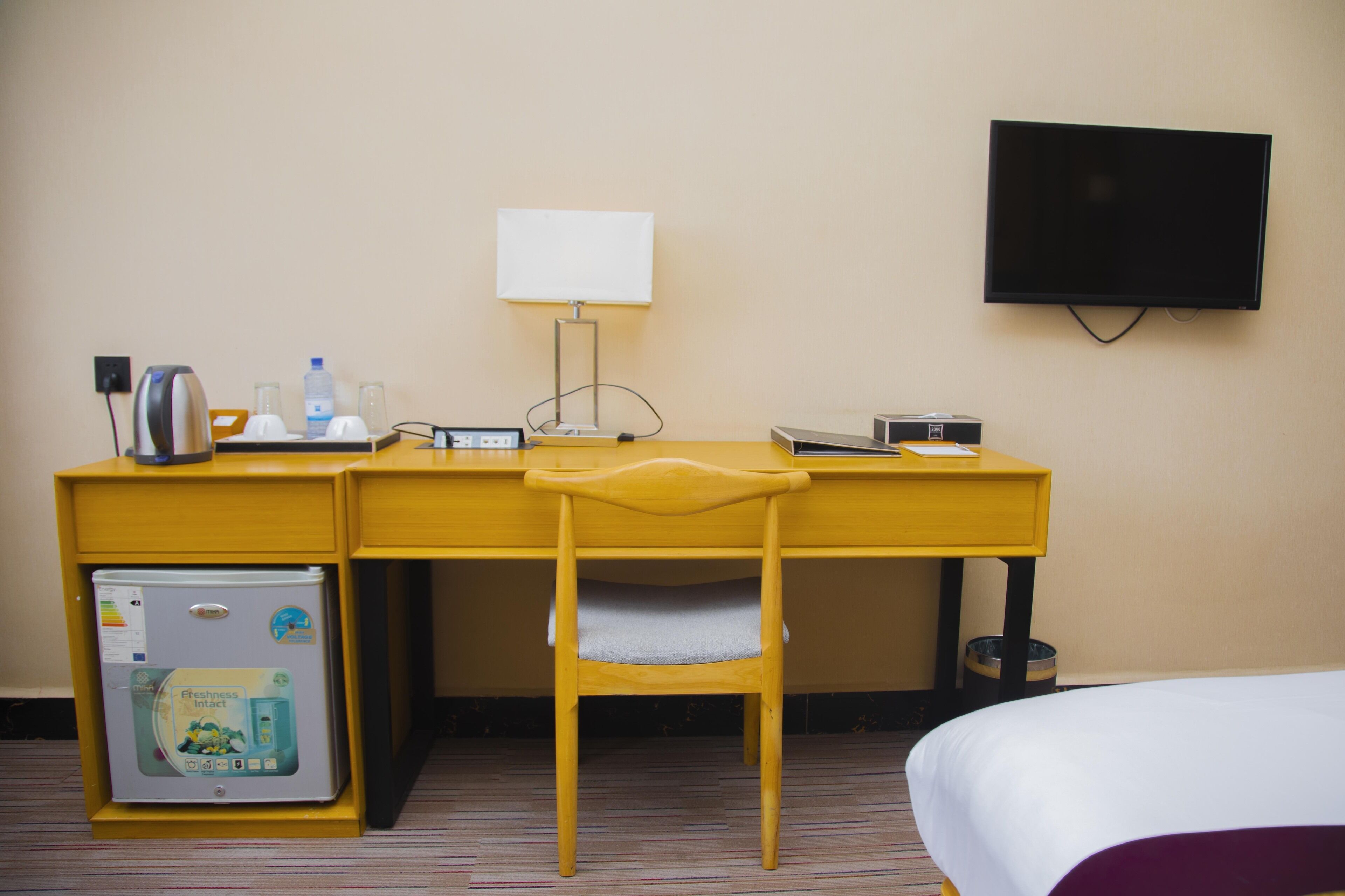 Habitación de hotel con escritorio, silla, cama, televisor, refrigerador y dispensador de agua.