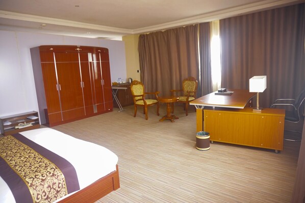 A hotel room with a bed, a desk with chairs, a wardrobe, and a window with curtains.