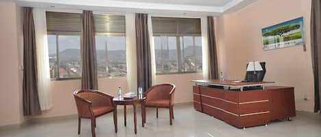 A hotel room with a dining area, a desk, and a large window with curtains.