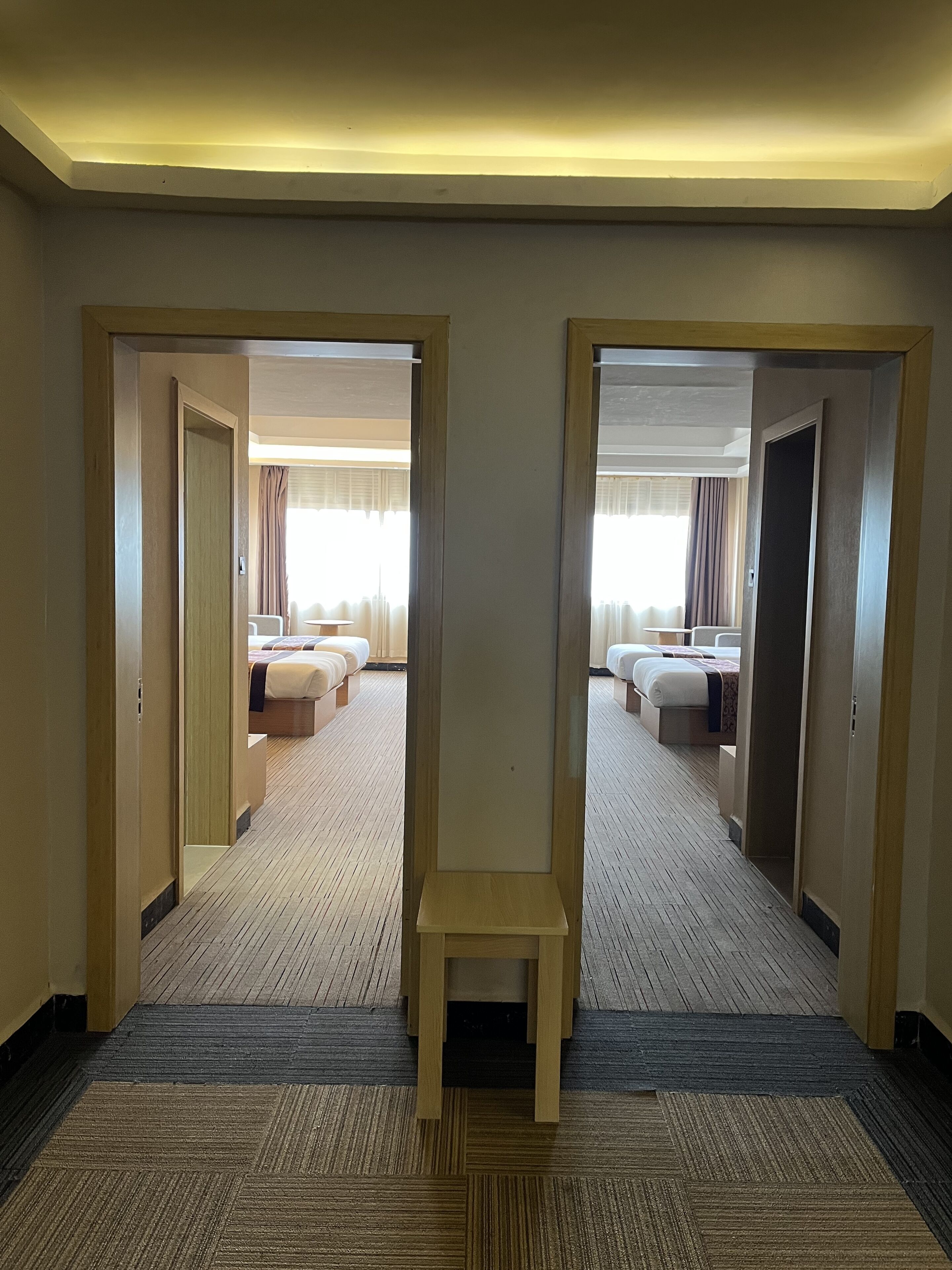 A hotel corridor with two doors leading to a room with two beds and a small table.