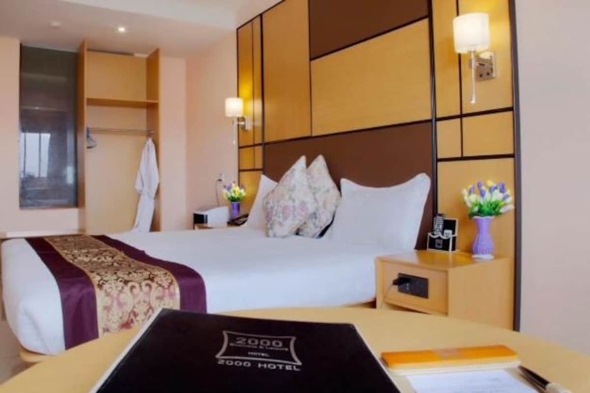 A hotel room with a large bed, a bedside table with a lamp, and a small table with a notebook and pen.