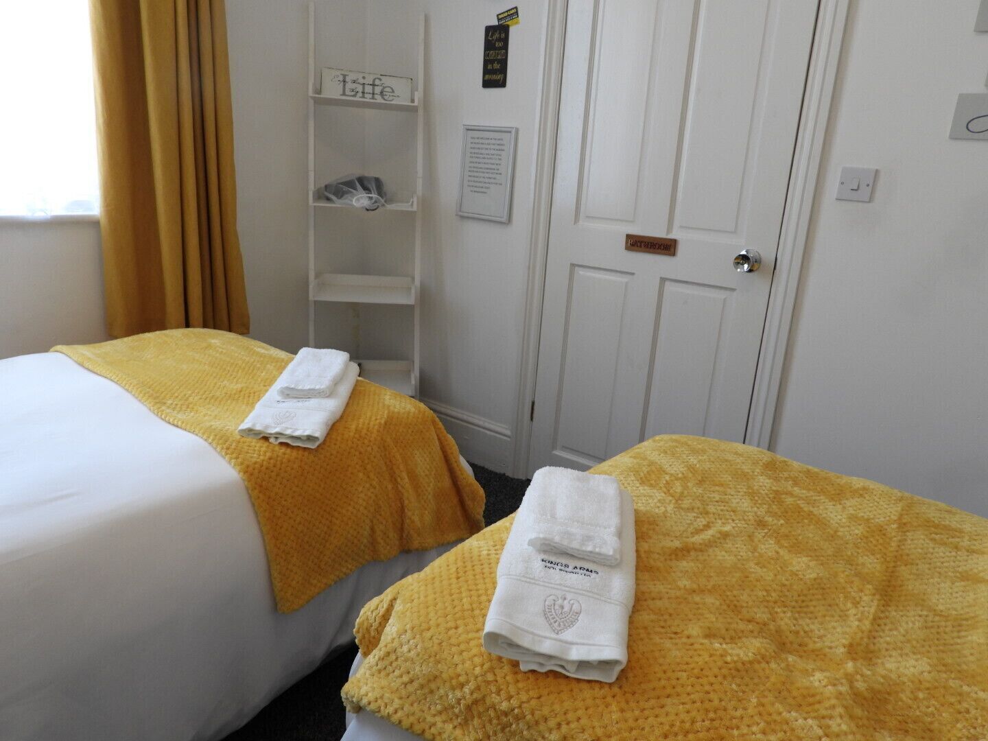 Two single beds with yellow blankets and white towels, a white wardrobe, and a shelf with a sign.