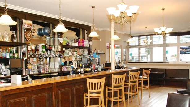 A bar area with wooden chairs, a bar counter, and various bottles and glasses. - Kings Arms Hotel (Holsworthy)