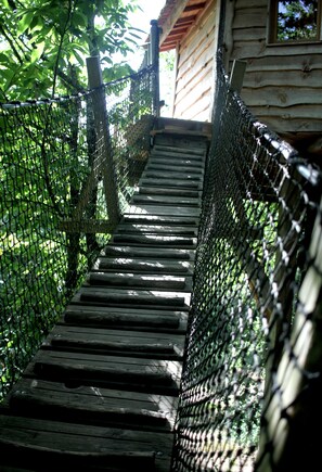 A wooden staircase leading up to a cabin with a wooden exterior and a netted enclosure on either side.