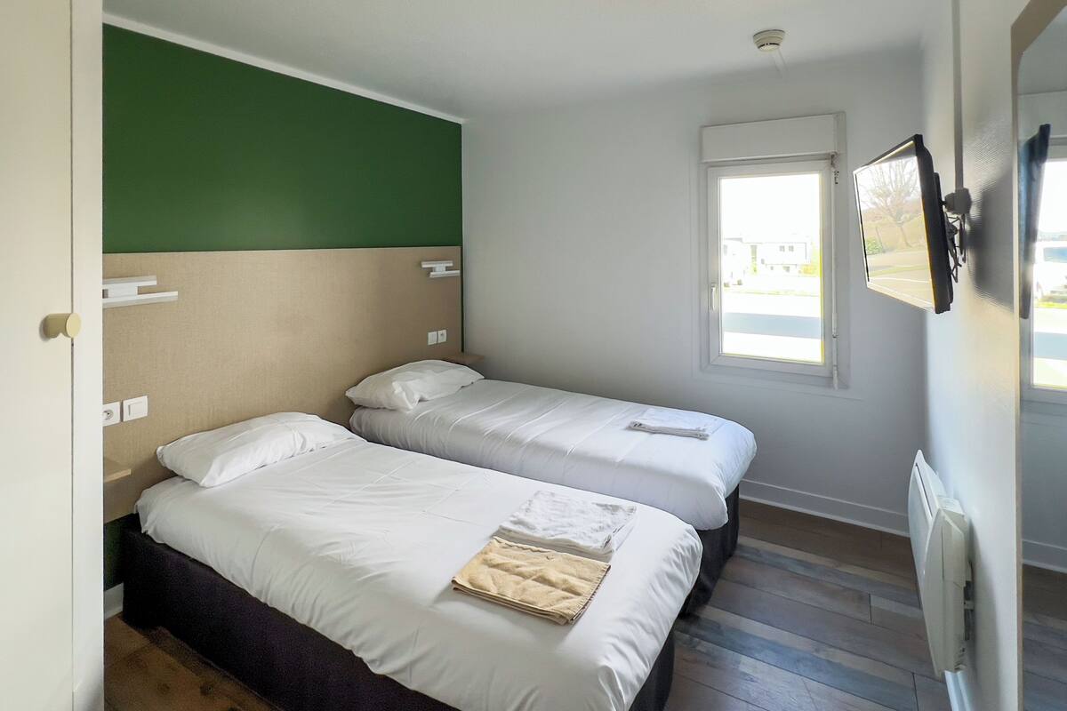 A room with two beds, a green wall, a window, and a radiator.