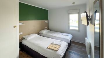 A room with two beds, a green wall, a window, and a radiator.