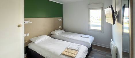 Una habitación con dos camas, una pared verde, una ventana y un radiador.