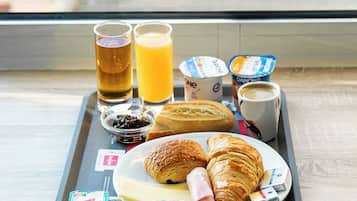 Ein Tablett mit Frühstücksartikeln, darunter Croissants, Käse, Schinken, Saft und Kaffee, auf einer Fensterbank.