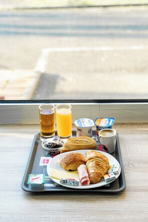 Una bandeja con alimentos para el desayuno, incluyendo cruasanes, queso, jamón, jugo y café, colocada en un alféizar.