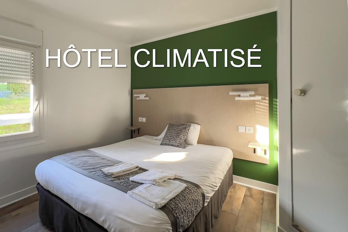 A hotel room with a bed, a window with blinds, and a green accent wall.
