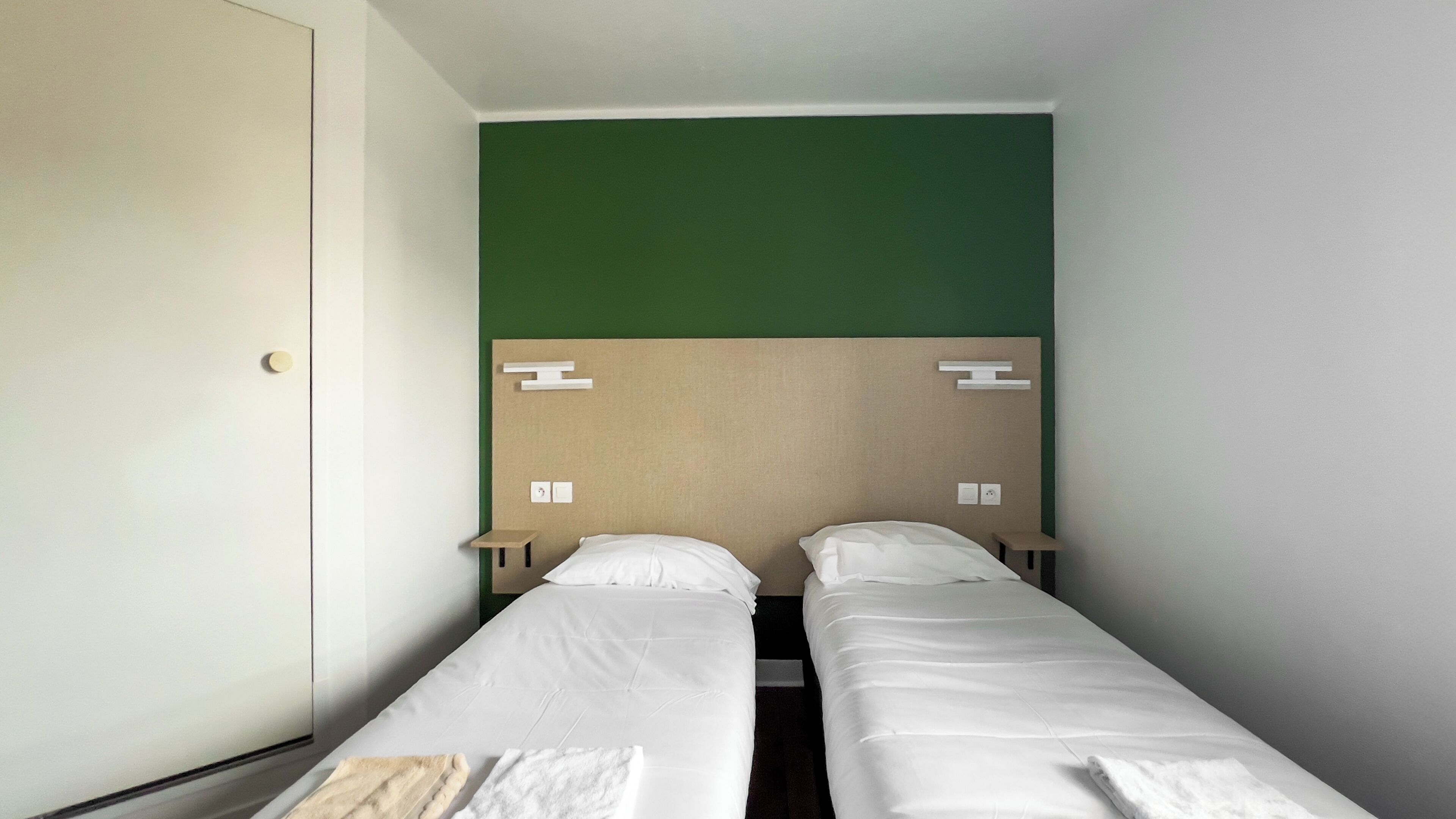 Habitación doble con dos camas individuales, una pared de acento verde y un cabecero de madera.