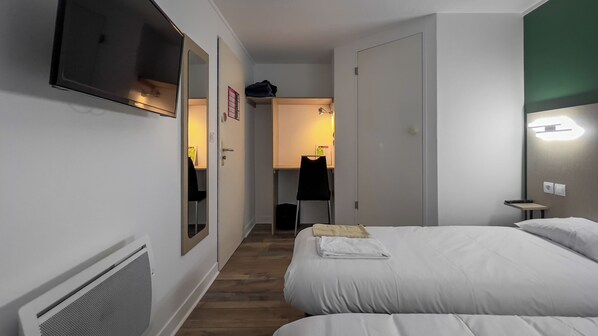 Una habitación de hotel con cama, escritorio, silla, espejo y televisor.