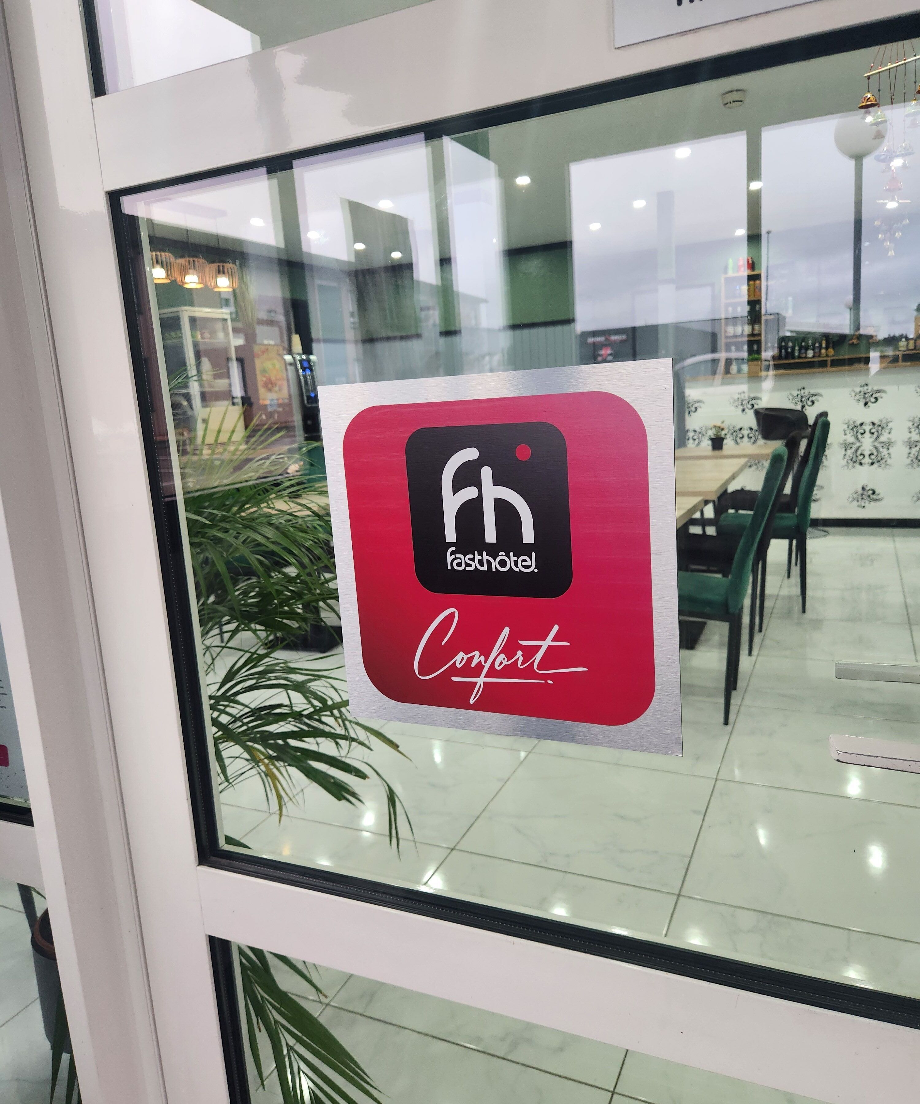 Un letrero con el logotipo 'fh' y la palabra 'Comfort' sobre un fondo rojo, colocado en una ventana de vidrio.