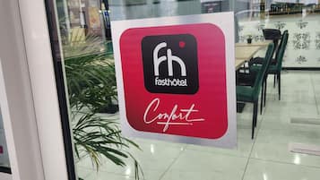 Un letrero con el logotipo 'fh' y la palabra 'Comfort' sobre un fondo rojo, colocado en una ventana de vidrio.