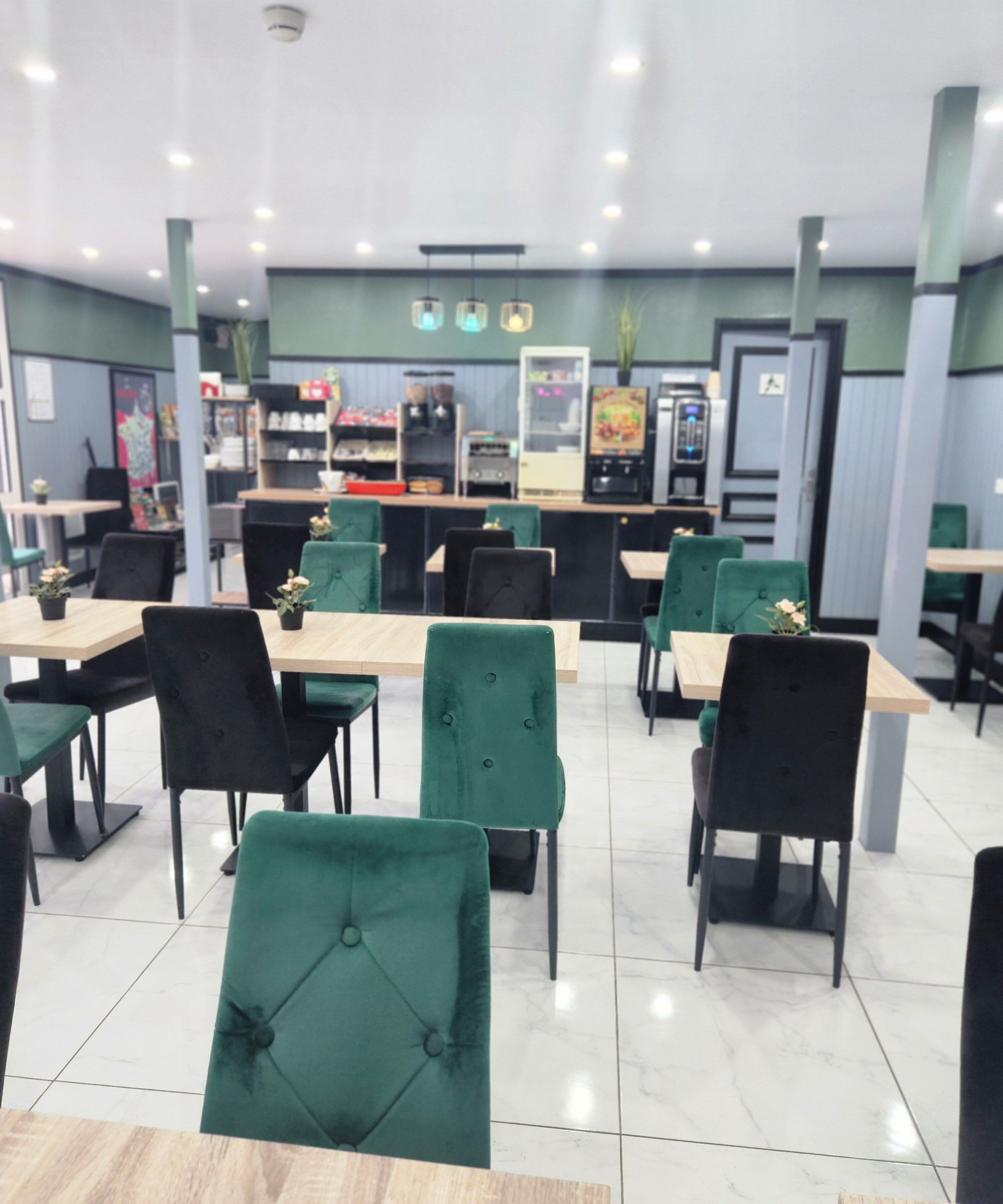 Een restaurant met groene beklede stoelen, houten tafels en een toonbank met diverse producten.