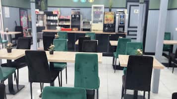 Een restaurant met groene beklede stoelen, houten tafels en een toonbank met diverse producten.