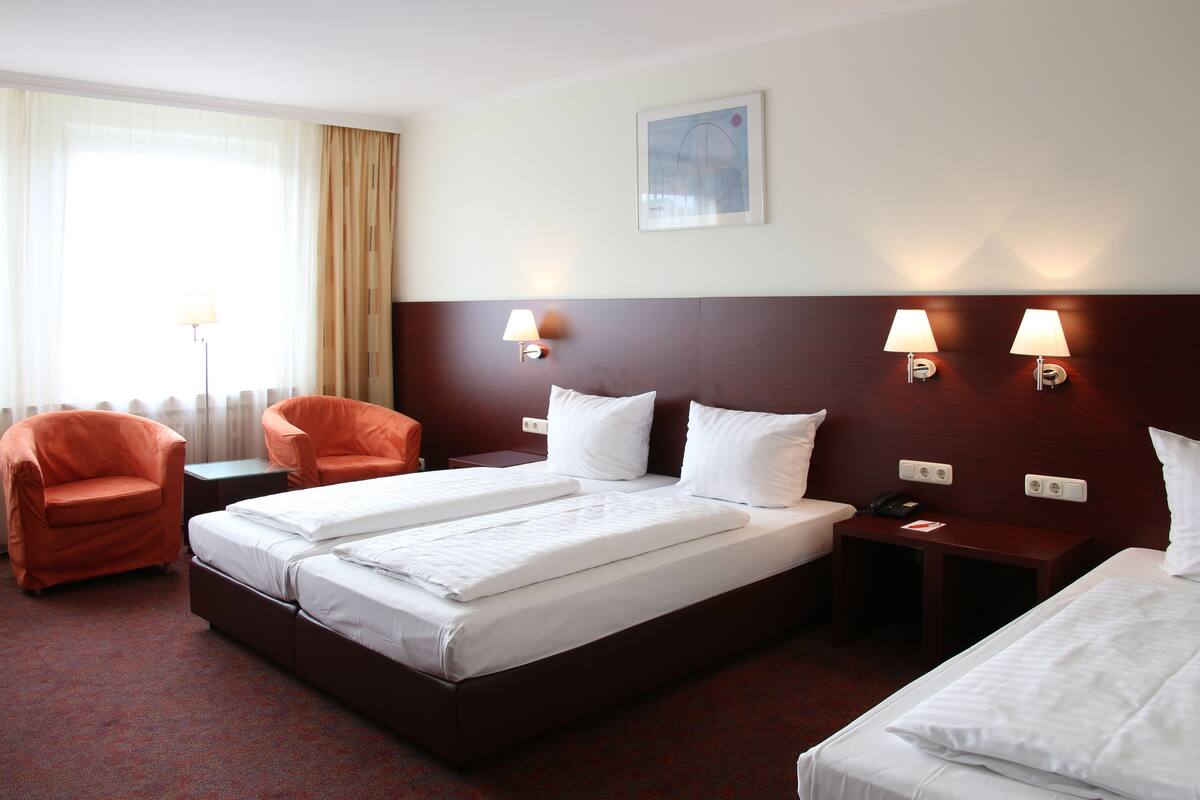 A hotel room with a large bed, two bedside tables, a desk, two chairs, and a window with curtains.