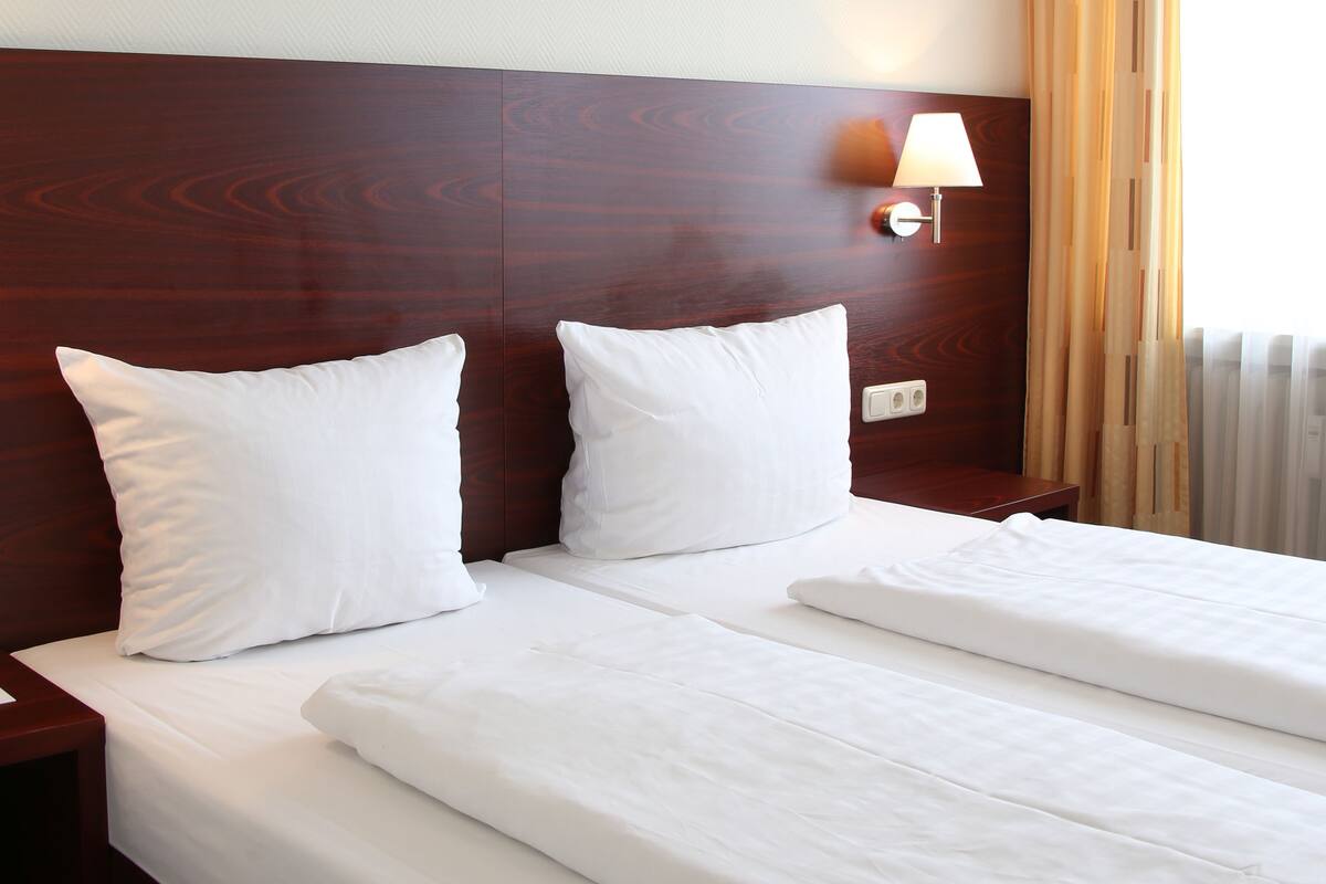 A hotel room with a double bed, a wooden headboard, a bedside lamp, and a framed artwork on the wall.