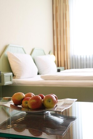 A bed with white bedding and green headboards, a bedside table with a glass top, and a plate of apples.