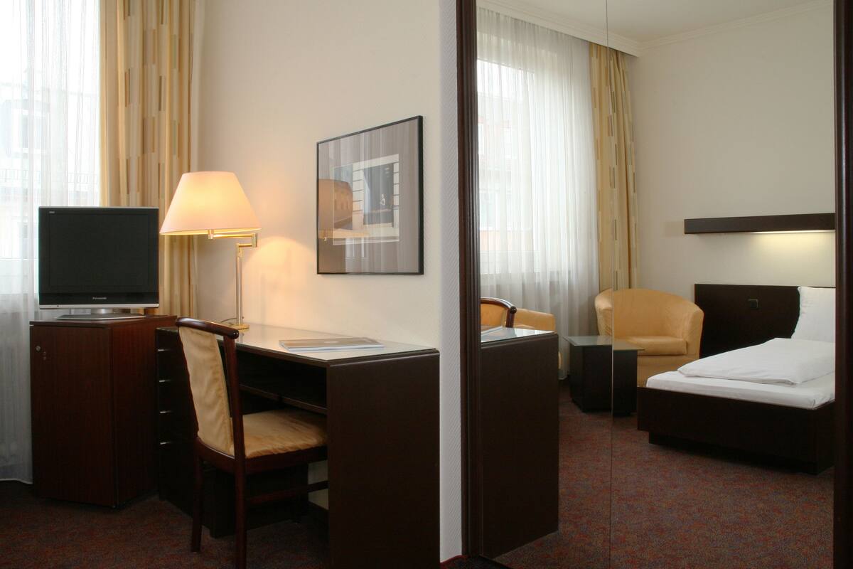A hotel room with a desk, chair, bed, and a television.
