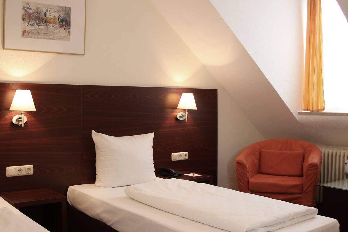 A hotel room with two beds, a wooden headboard, two bedside lamps, a framed picture on the wall, and a window with curtains.