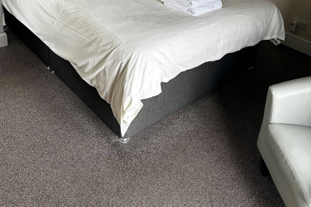 A hotel room with a large bed, a black headboard, a radiator, and a white chair.