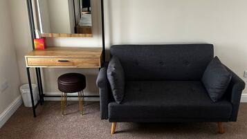 A room with a dark grey sofa, a wooden desk with a mirror, and a small stool.