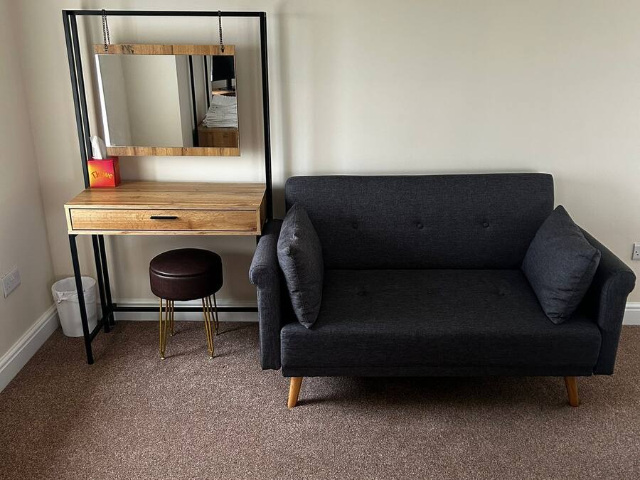 A room with a dark grey sofa, a wooden desk with a mirror, and a small stool.