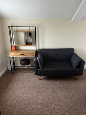 A room with a dark grey sofa, a wooden desk with a mirror, and a small stool. - Chevin End Guest House (Ilkley)
