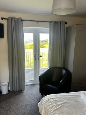 A hotel room with a bed, a chair, a wardrobe, and a balcony with curtains. - Chevin End Guest House (Ilkley)