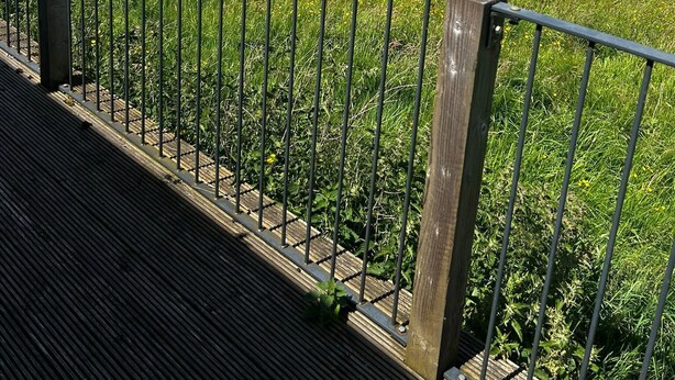 A scenic view from a balcony with a metal railing, overlooking a grassy field with scattered trees and a distant town. - Chevin End Guest House (Ilkley)