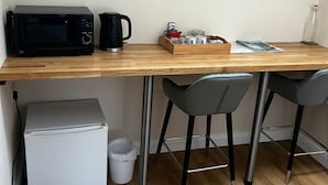 A kitchenette with a microwave, coffee maker, and a small refrigerator. There are two chairs and a tray with cups and a bottle. - Chevin End Guest House (Ilkley)